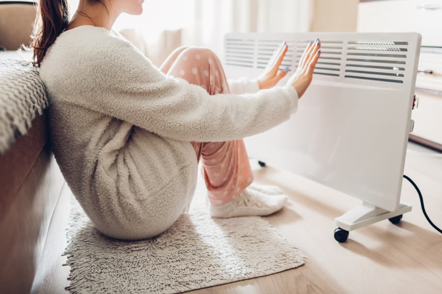 woman sitting on floor warming up in front of a space heater
