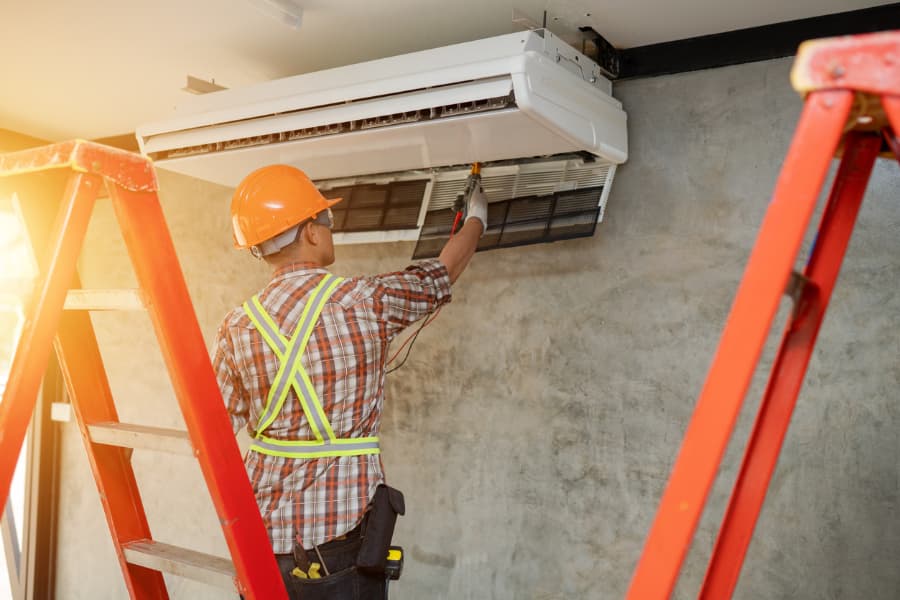 Worker on ladder fixing air conditioning unit